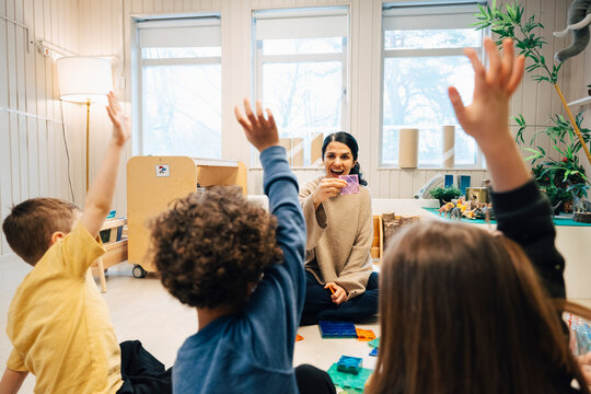 Happy female teacher doing fun group activity with elementary children sitting on classroom floor