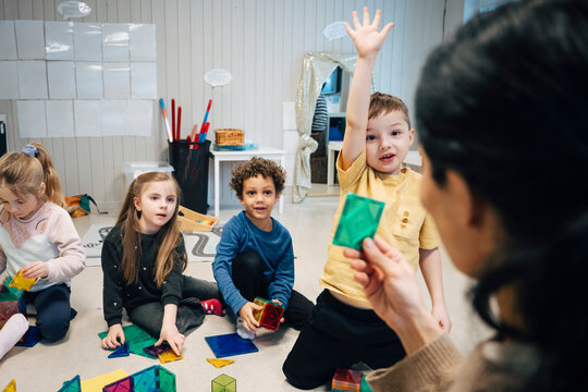 Cute boy raising hand and answering during interactive session in classroom