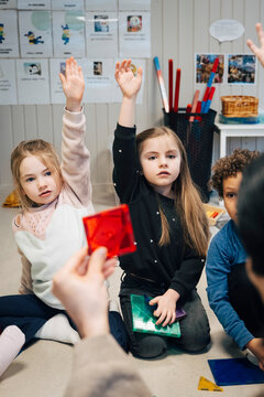 Cute girls raising hands and answering during play-based learning in classroom