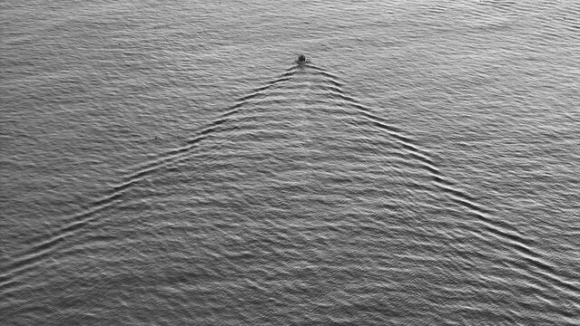 Aerial view of a single, solitary boat sits amidst the rippling expanse of the ocean, its presence marked by symmetrical waves, Carantec, Brittany, France.
