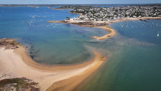 Aerial view of the vivid turquoise sea meeting the sandy beach and rocky coastline, boats dotting the horizon, Carantec, Brittany, France.