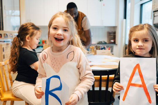 Playful kindergarten students holding hand drawn alphabet cards in classroom