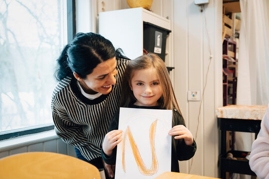 Portrait of happy teacher looking at girl showing hand drawn alphabet card in classroom