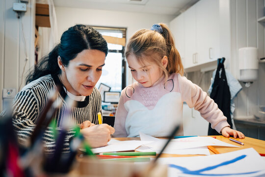 Female teacher guiding kindergarten student through drawing activity in class