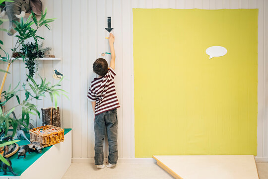 Rear view full length of boy touching arrow symbol on wall with yellow backdrop in classroom