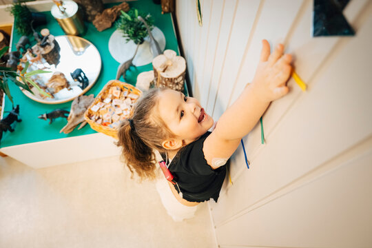 High angle view of girl sticking out tongue while trying to touch arrow on wall at preschool