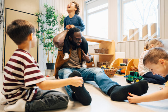 Group of boys tickling male teacher sitting on classroom floor