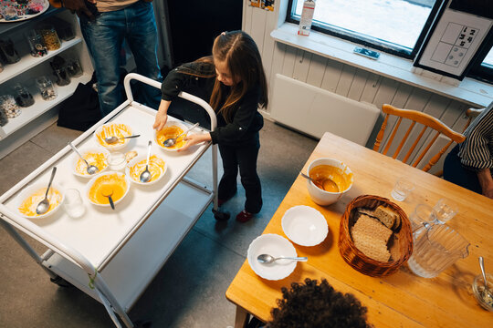High angle view of girl keeping soup bowl on cart during lunch break at preschool