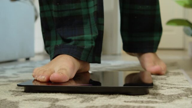 Close-up of a man's bare feet stepping onto a modern digital weighing scale in the morning at home. Healthy lifestyle, weight control and body awareness concept, soft natural light 4K.