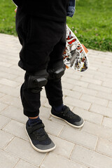 Cropped shot of a child holding a white penny board with orange wheels while standing on a dark grey rubberized playground surface, low angle view for extreme sports, childhood, and active lifestyle
