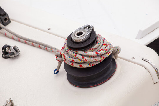 Closeup of a sailboat winch with a coiled rope on the white deck. Detail of yacht rigging for sailing, adventure, and marine sport.