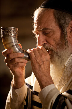Close-up of an elderly Jewish man blowing a shofar with a shallow depth of field in a warm and spiritual mood.