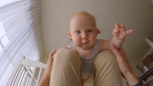 Father gently bouncing his six-month-old baby on his knees, filmed from the father's point of view. Tender bonding moment, childcare routine and loving parenthood. Slowmoton video.