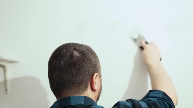 Handyman filling holes on white wall with putty knife, wall preparation process, high quality 10 bit 4K.
