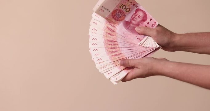 Hand holding fanned stack of Chinese yuan banknotes, close up, beige background. Hand, yuan, banknotes, fanned, stack, beige, close up