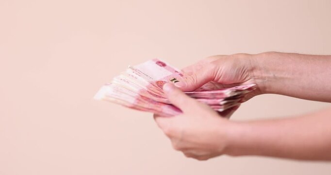 Hand holding fanned stack of Chinese yuan banknotes, close up, beige background. Hand, yuan, banknotes, fanned, stack, beige, close up