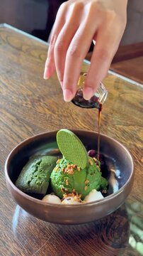 Pouring dark syrup over Japanese matcha green tea ice cream dessert bowl in a cafe