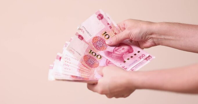 Hand holding fanned stack of Chinese yuan banknotes, close up, beige background. Hand, yuan, banknotes, fanned, stack, beige, close up
