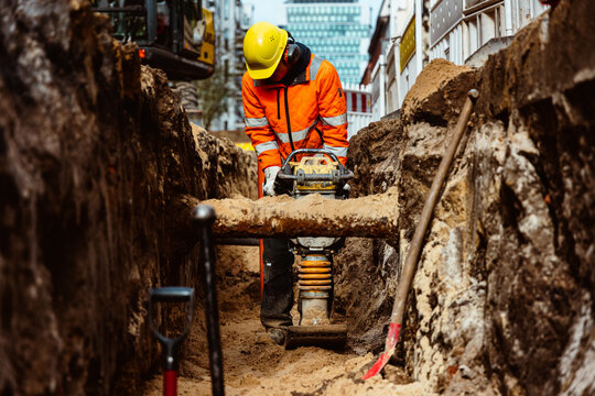 Bauarbeiter mit R&uuml;ttelplatte im Graben