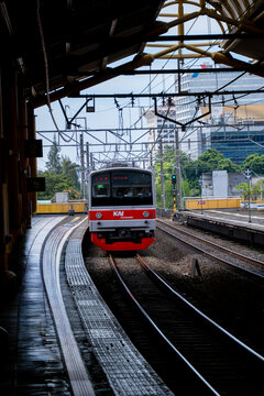 Jakarta, Indonesia - March 24, 2026: KAI Commuter train arriving at Gondangdia Station platform, framed by urban buildings and overhead power lines.