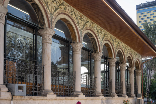 Detailed view of the Et'hem Bej Mosque's portico in Tirana, Albania, featuring richly painted Ottoman-era arches, carved stone columns, and modern glass reflections.