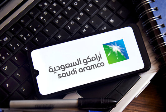 Saudi Aramco logo on a smartphone screen with office objects in the background. It is the world's largest oil company in reserves, production and profitability, headquartered in Dhahran, Saudi Arabia.