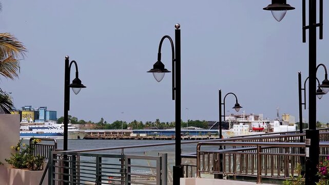 Mattancherry's promenade unfolds through the watchful eyes of black lamp posts. Framed by these iron sentinels, a docked ship sits upon the water, palm trees, distant buildings lining the kochi shore.