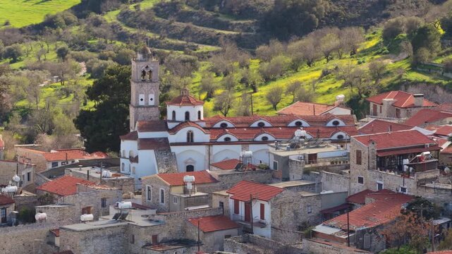 Aerial drone view of a traditional Cypriot village featuring a historic church with bell tower and red tiled roofs. Pano Lefkara, Cyprus