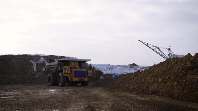 Yellow Mining Dump Truck Being Loaded by Excavator at Open Pit Coal Mine in Winter. Walking Dragline Excavator in Background at a Snowy Mining Site.