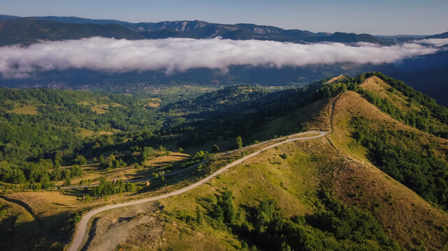 Aerial view of mountain ridge with winding road and low clouds over green valley at sunrise
