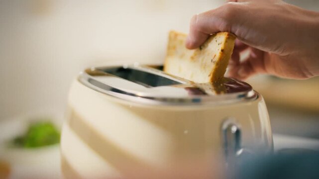 A hand places a slice of bread into a toaster, preparing for a breakfast. The kitchen setting is warm and inviting, capturing a moment of daily life in the morning