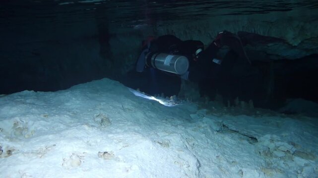 Technical diver exploring a submerged cave with stalactites and following a guideline