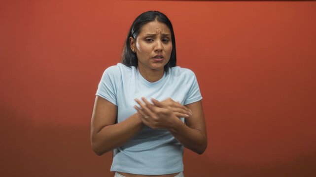 Woman holds arms across chest, hands clasped and shivering in a studio, wearing blue tshirt and visible rings on fingers; anxiety vulnerability.