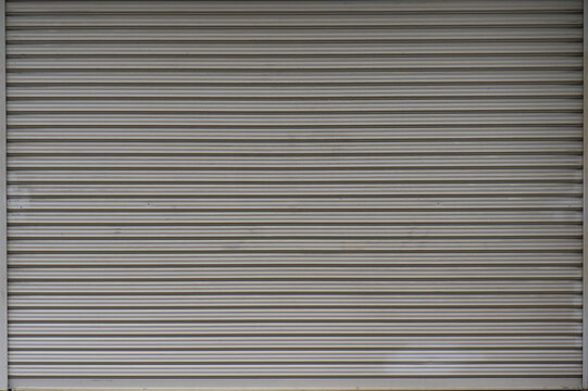 Horizontal texture of gray metal roller shutter door. Industrial silver steel background for minimalist design, security, and urban architecture concept.