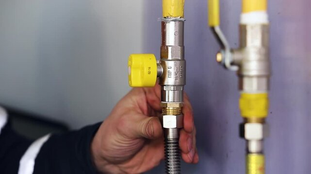 Gas Technician Connecting Flexible Hose to Yellow Gas Pipe Valve on Wall. Plumber Installing Gas Appliance Connection During Home Gasification.