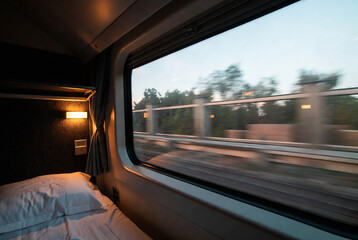 Fototapeta premium A sleeping compartment on a train with a view of passing trees and fields outside.