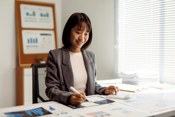 Asian businesswoman working efficiently in an office, managing calculations and financial charts for business analysis and planning