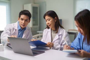 Healthcare professionals having a meeting, discussing patient information using a laptop, and taking notes in a clinic