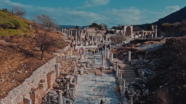 Elevated view of the ancient marble road in Ephesus, Izmir, Turkey. Ruins, columns, stone structures, hills and visitors create a scenic archaeological landscape rich in history and heritage.