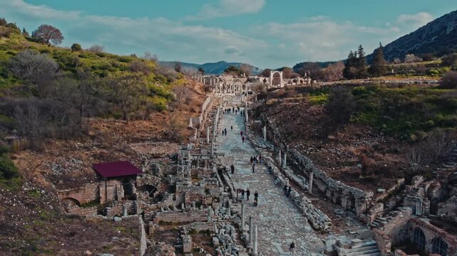 Tourists walk along the ancient marble street in Ephesus, Izmir, Turkey. Historic columns, stone road, archaeological ruins and scenic hills create a timeless travel and heritage atmosphere.