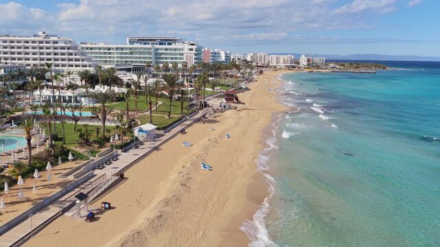 Aerial drone view of a sandy beach lined with modern hotels and palm trees, near Fig Tree Bay, Protaras, Cyprus