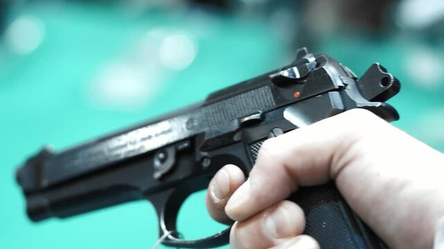 close-up of a person holding a handgun.

Key details:
The firearm appears to be a semi-automatic pistol, held firmly in one hand.
The person&rsquo;s finger is inside or near the trigger guard, suggesting re