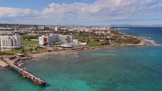 Aerial drone view of a small pier extending into clear turquoise waters along the coastline of Protaras