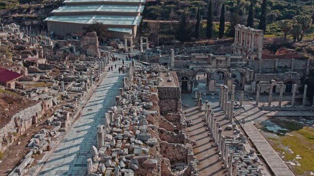 Tourists walk along the ancient marble street in Ephesus, Izmir, Turkey. Historic columns, stone road, archaeological ruins and scenic hills create a timeless travel and heritage atmosphere.