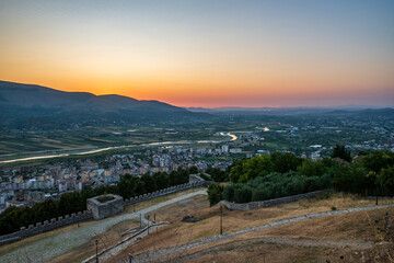 Obraz premium A sweeping sunset panorama from Berat Castle showcases the city, winding Osum River, and fertile agricultural valley stretching to distant mountains in Berat, Albania.