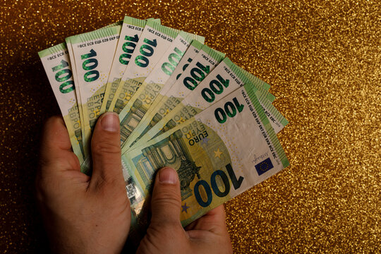 Person showing off a fan of 100 Euro bills with a sparkling gold background. Concept of wealth, fina