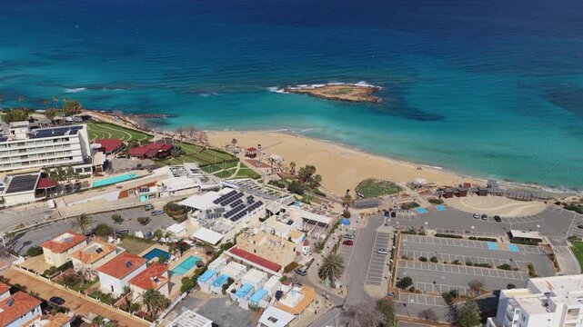 Aerial drone view of a sandy beach and turquoise sea in Protaras, Cyprus, featuring a small offshore islet near Fig Tree Bay