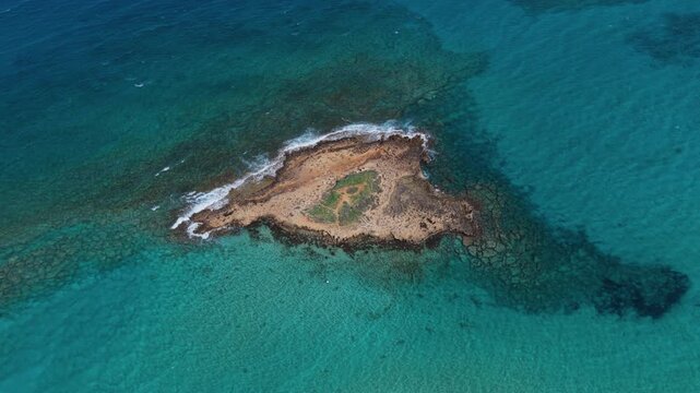 Aerial drone view of a small rocky island surrounded by clear blue water in Protaras, Cyprus, near Fig Tree Bay