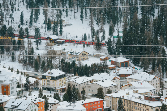 Red train passing a snow covered village in the swiss alps