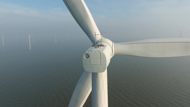 Aerial drone view of offshore wind turbines in the sea covered in thick fog. Industrial wind farm generators in misty ocean water. Concept of renewable energy, mysterious weather and green power. 
